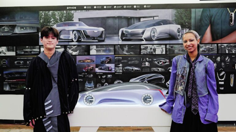 Students standing and smiling in front of a display of modern industrial designs.