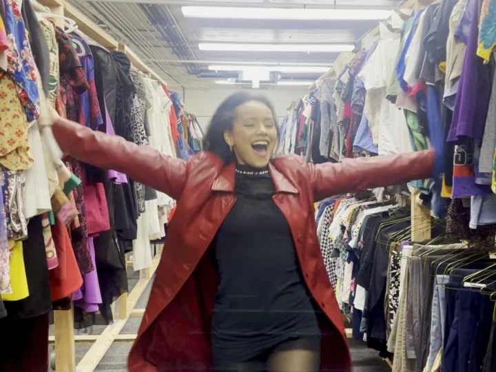 Student with open arms in a room full of costumes and various clothing